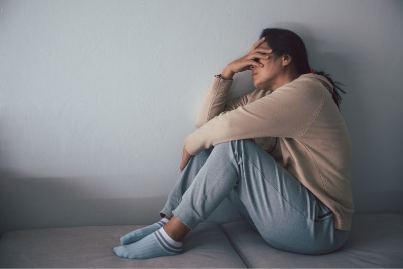 Mujer sentada en el suelo, visiblemente angustiada y sosteniendo su cabeza en señal de sufrimiento.