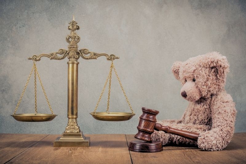 Oso de peluche sentado frente a una balanza de la justicia y un mazo judicial