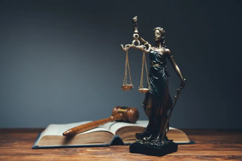 Figura de la justicia con balanza en un escritorio junto a un libro abierto y un mazo judicial, representando los principios del derecho y la reforma del Código Penal español.