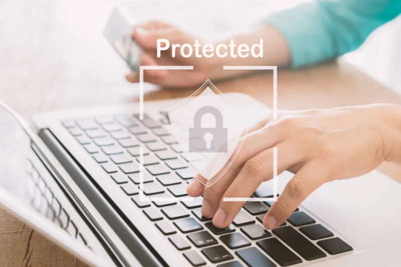 Manos sobre teclado de laptop con ícono de seguridad digital y la palabra "Protected"