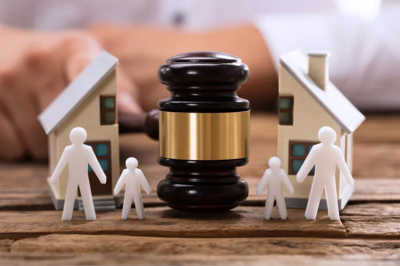 Símbolo de justicia representado por un mazo judicial entre figuras de familia dividida y casas, simbolizando un divorcio conflictivo.