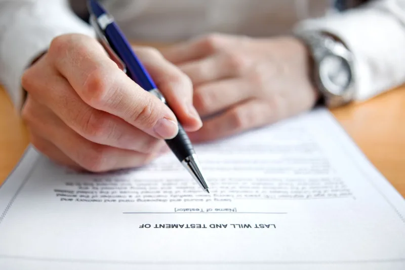 Cómo Impugnar un Testamento: Mano firmando un documento titulado "Last Will and Testament" con bolígrafo.