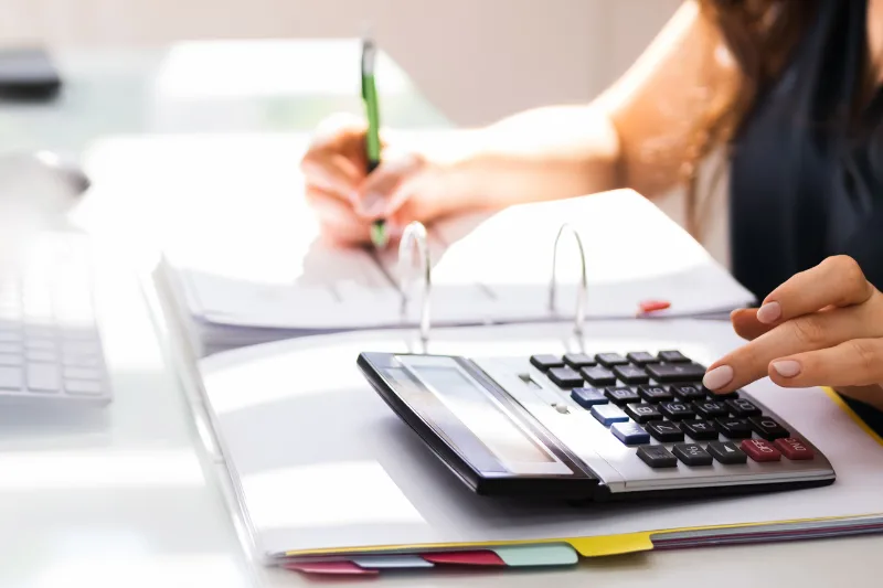 Persona calculando impuestos con una calculadora y documentos contables.