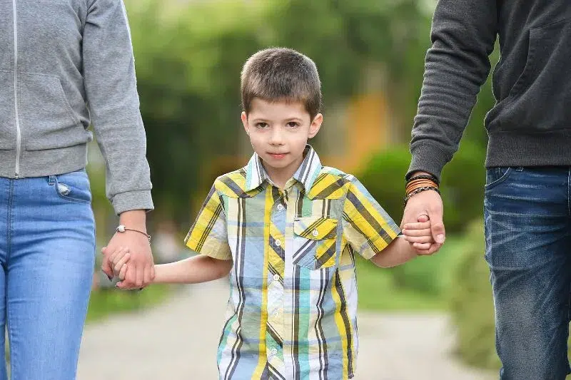 Niño caminando con ambos padres tomados de la mano, simbolizando la custodia compartida y la cooperación familiar.