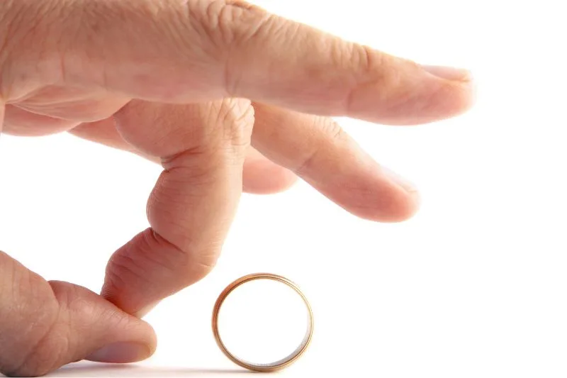 Mano de una persona empujando un anillo de matrimonio, simbolizando el divorcio y la pérdida de derechos hereditarios.