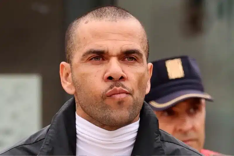 Primer plano de Dani Alves con rostro serio, escoltado por un agente de policía