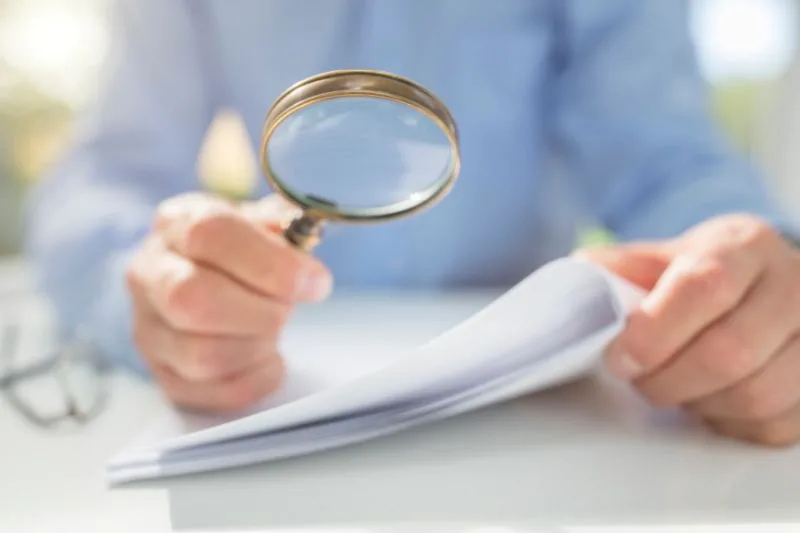 Hombre revisando documentos con lupa por posible falsedad documental