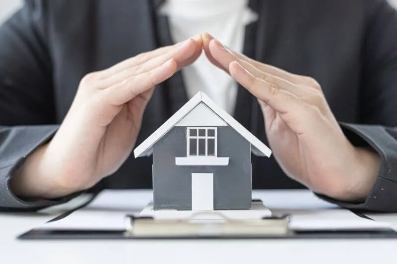 Manos protegiendo una casa en miniatura como símbolo legal contra ocupación ilegal de viviendas en verano
