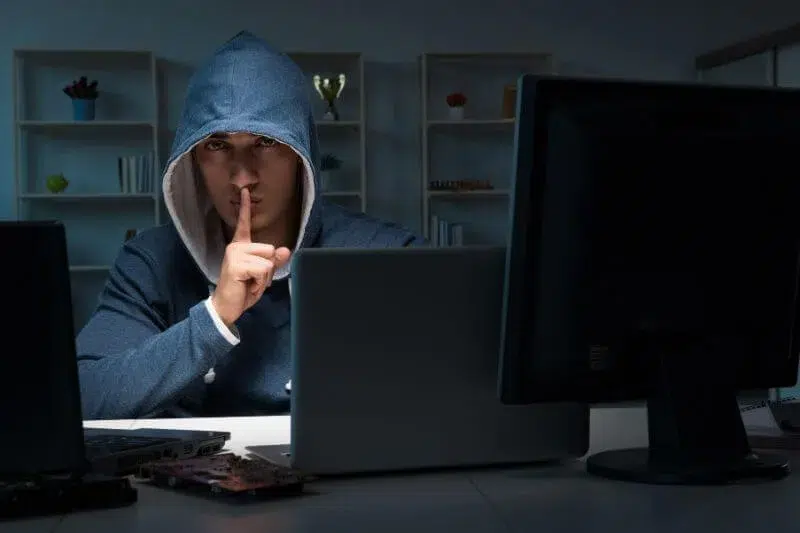 Individuo con capucha realizando suplantación de identidad en internet frente a varios ordenadores